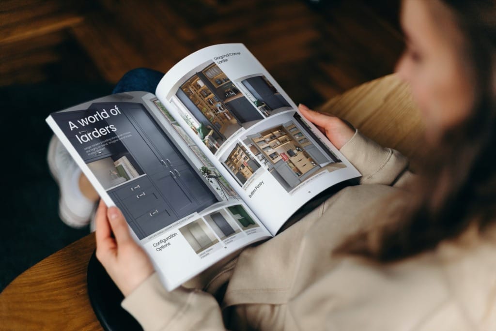 A person browsing through a beautifully designed kitchen brochure, featuring high-quality images and layouts showcasing various kitchen styles and designs. The open pages highlight bespoke cabinetry and elegant finishes, inspiring readers to imagine their own dream kitchen. The setting conveys a sense of relaxation and focus, reflecting the thoughtful process of planning a tailored kitchen with Mastercraft Kitchens