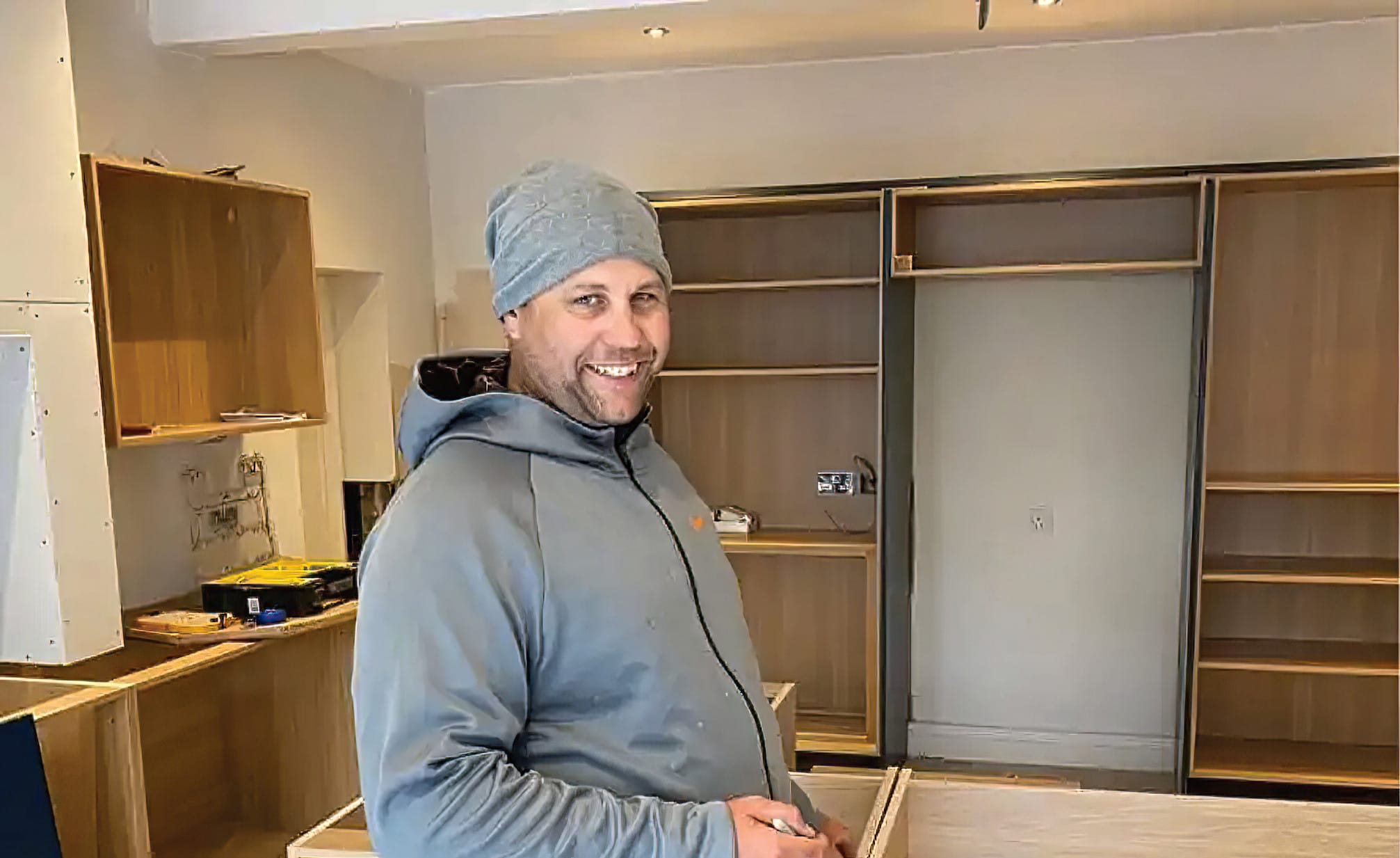 A skilled kitchen fitter smiling while working on a bespoke kitchen installation, showcasing the friendly professionalism and expertise of Mastercraft Kitchens. The partially assembled cabinets in the background highlight the high-quality materials and custom craftsmanship involved in creating a personalised kitchen. The relaxed and approachable demeanour of the fitter reflects the company’s commitment to excellent customer service and attention to detail throughout the installation process.