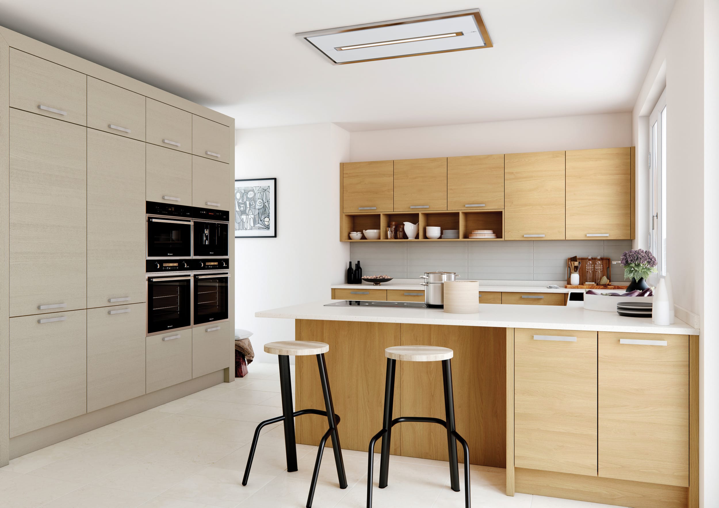 A modern kitchen with a clean and minimalist design, featuring a mix of light oak and soft beige cabinetry. The tall unit wall houses sleek, built-in black ovens and additional storage. A spacious island with a crisp white countertop doubles as a preparation area and breakfast bar, accompanied by two contemporary stools with light wooden seats and black metal legs. The upper cabinetry and open shelving display an arrangement of stylish crockery, adding warmth and character. The design is completed with a ceiling-mounted extractor fan, neutral tiled flooring, and natural light flooding in through a large window, creating a bright and airy space.